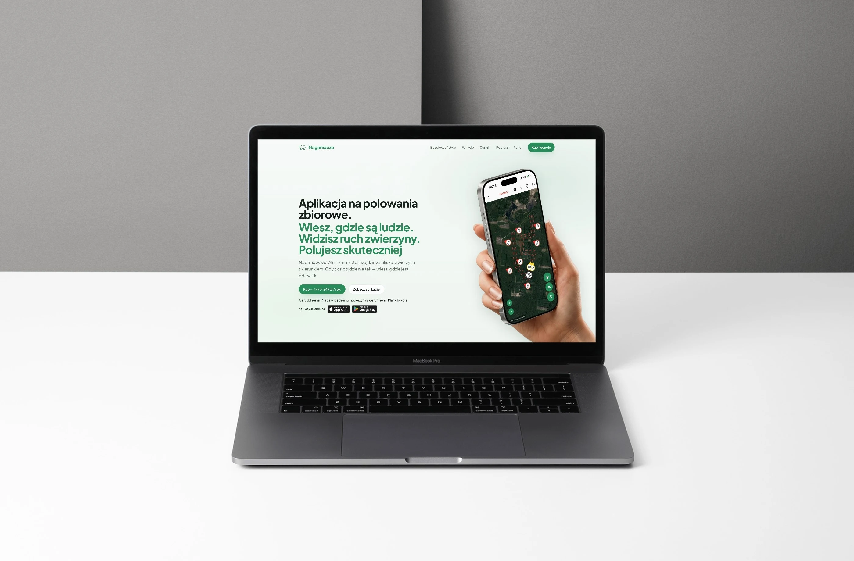 Strona naganiacze.app na laptopie: nagłówek „Aplikacja na polowania zbiorowe” i dłoń z telefonem
